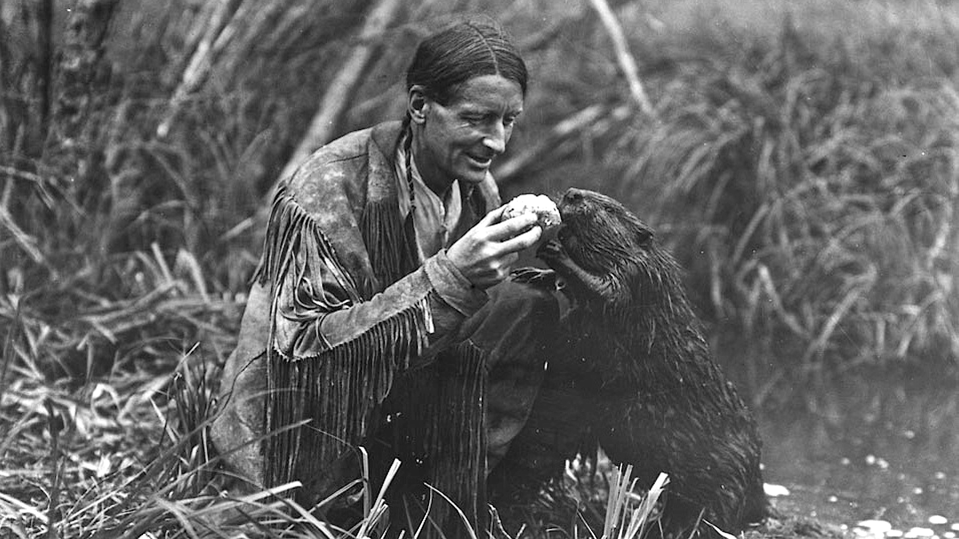 An outrageous man kneeling in the water with a beaver.