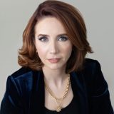 A woman wearing a black jacket and gold necklace.