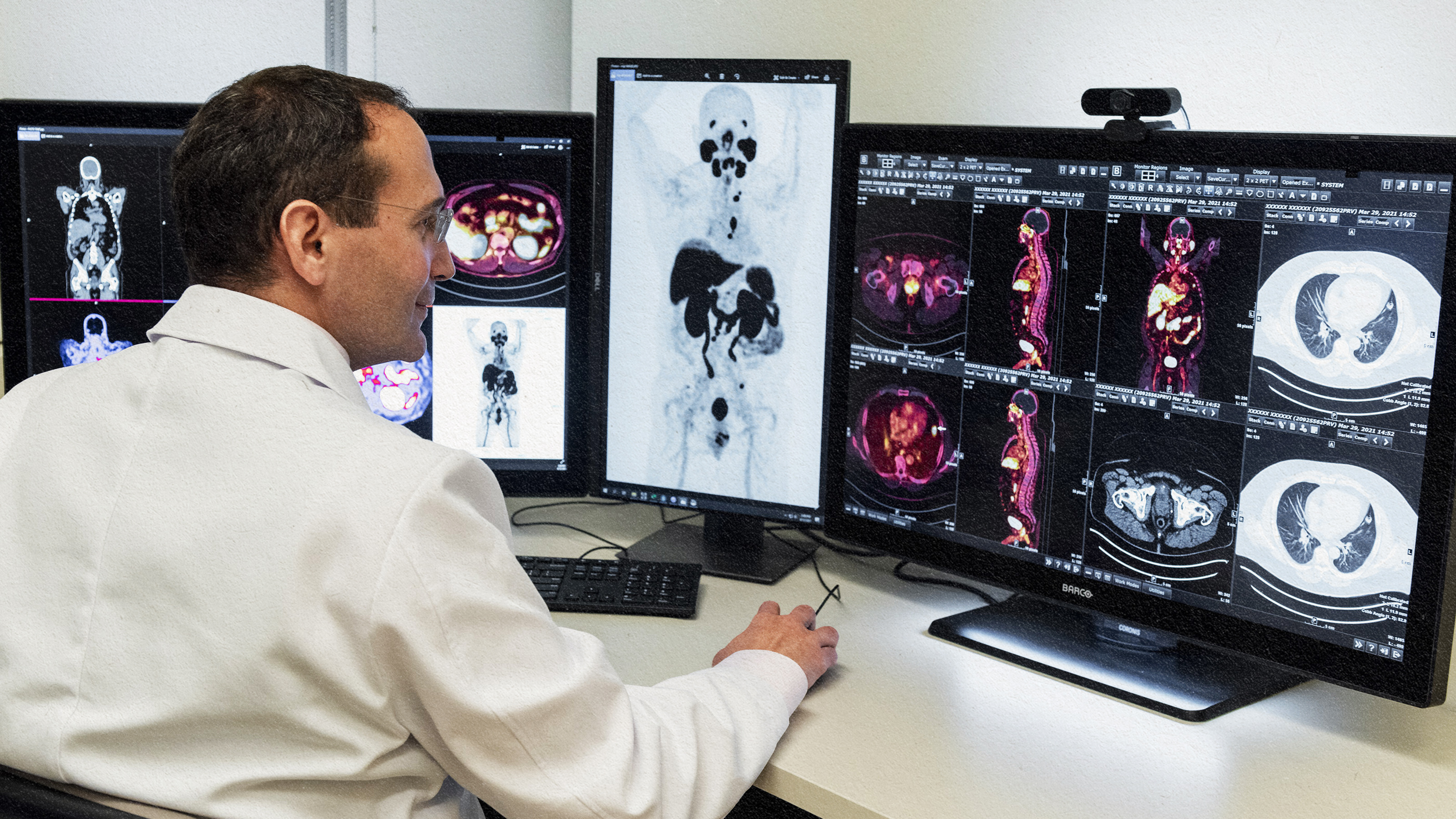 A man in a white coat is analyzing positron emissions on two monitors.