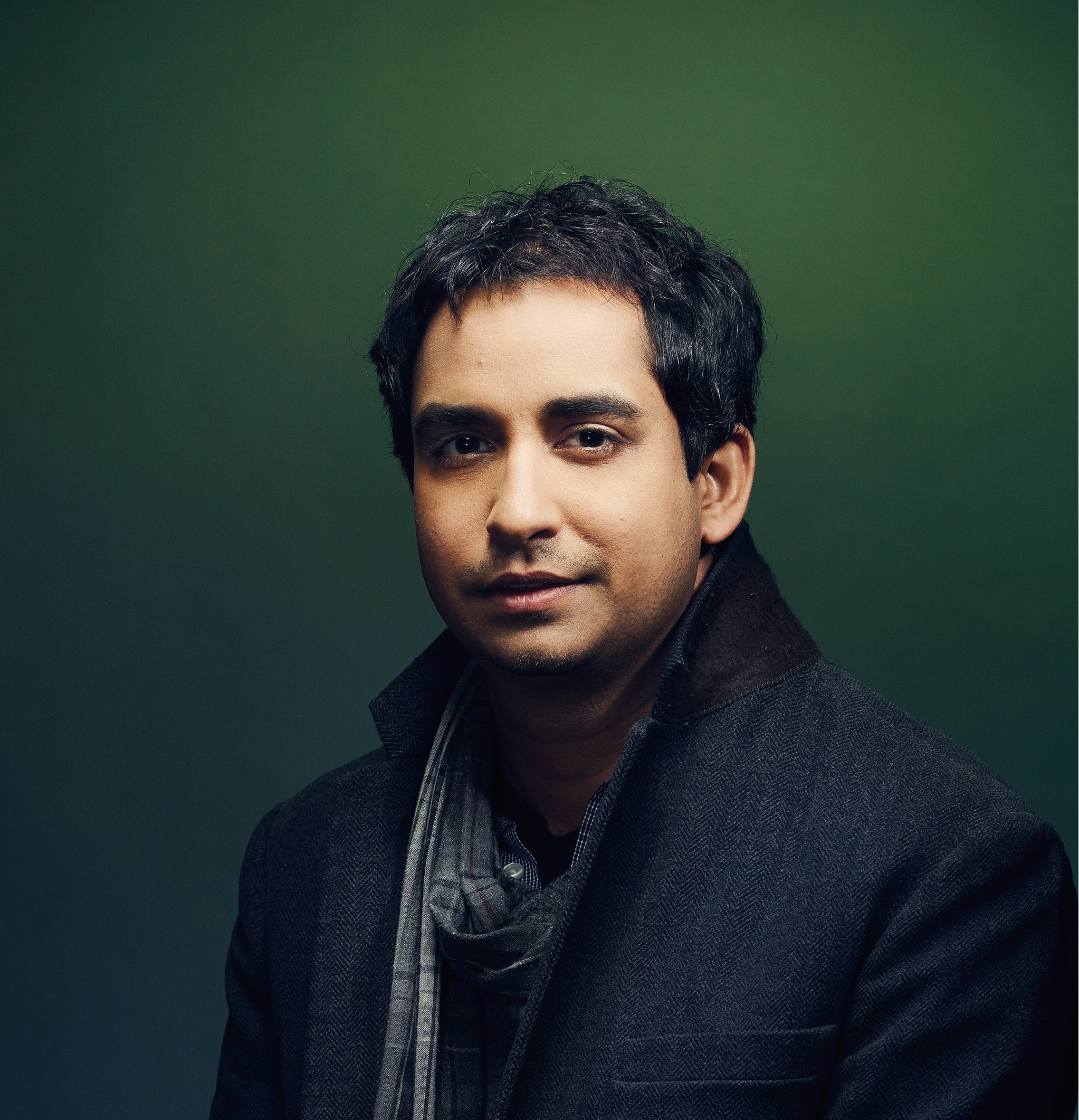 A man standing in front of a green background.