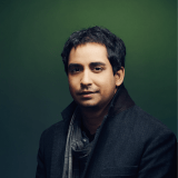 A man standing in front of a green background.