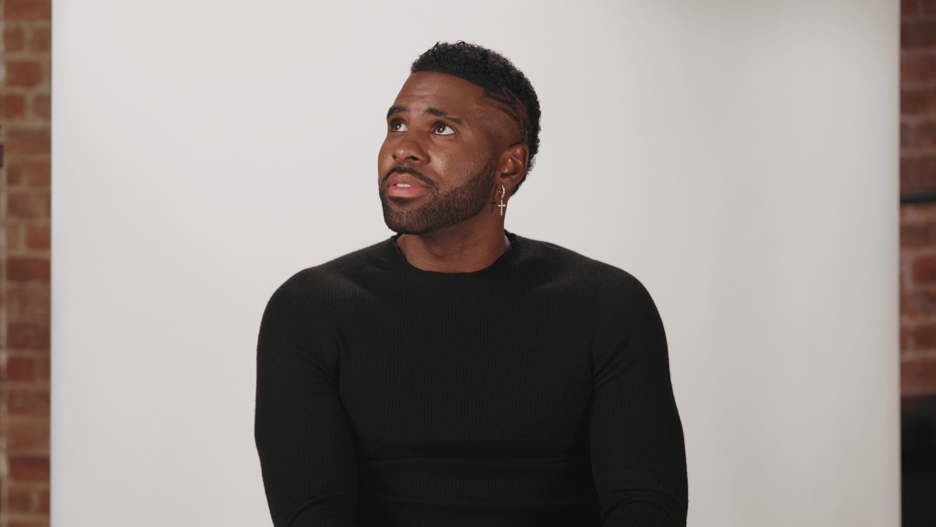A black man sitting in front of a brick wall.