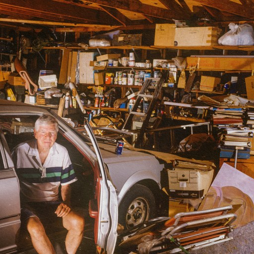 A man displaying signs of hoarding disorder, sitting in a car in a garage.