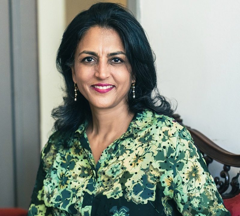 A woman in a green floral shirt sitting on a chair.