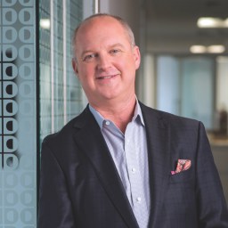 A man in a suit standing in front of a glass wall.