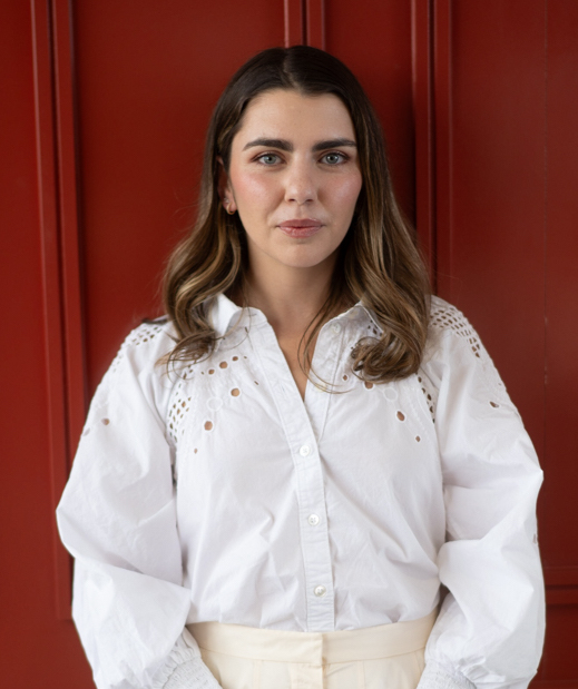 A woman in a white shirt and white pants standing in front of a red door.