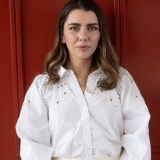 A woman in a white shirt and white pants standing in front of a red door.