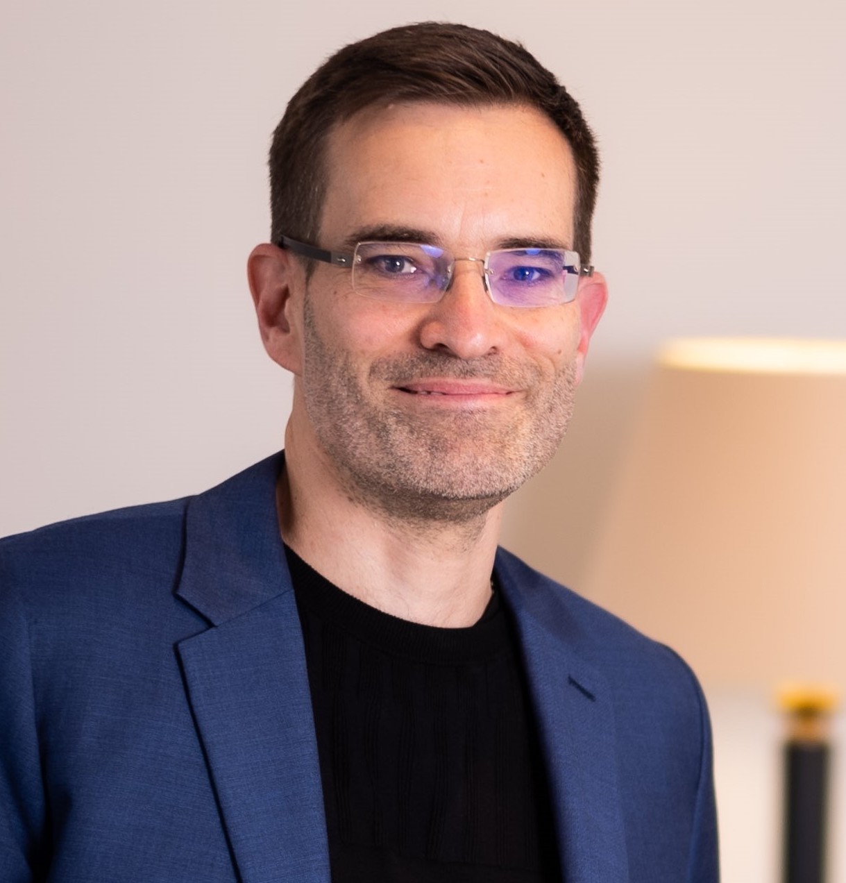 A man in glasses is smiling in front of a lamp.