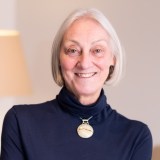 A woman in a blue turtle neck shirt smiling.