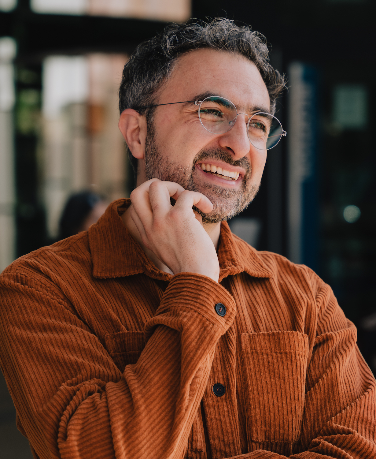 A smiling man wearing glasses and an orange shirt.