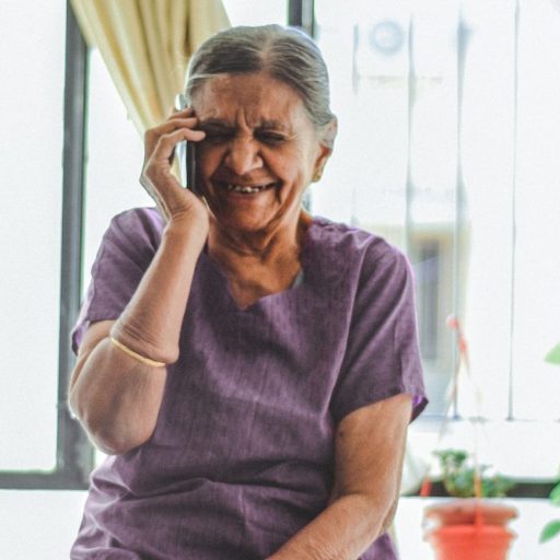 An elderly woman sitting on a chair and talking on the phone.