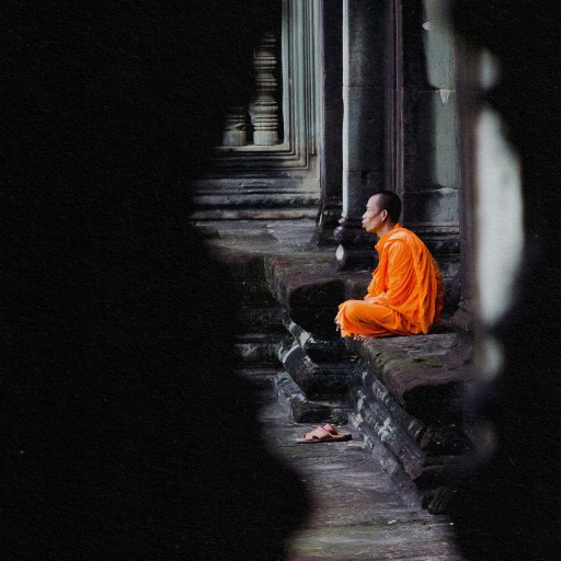 An orange-robed monk practicing mindfulness on a stone wall.