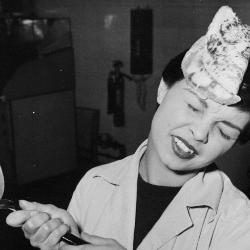 A woman holding a frying pan with an intelligently failed pizza on it.