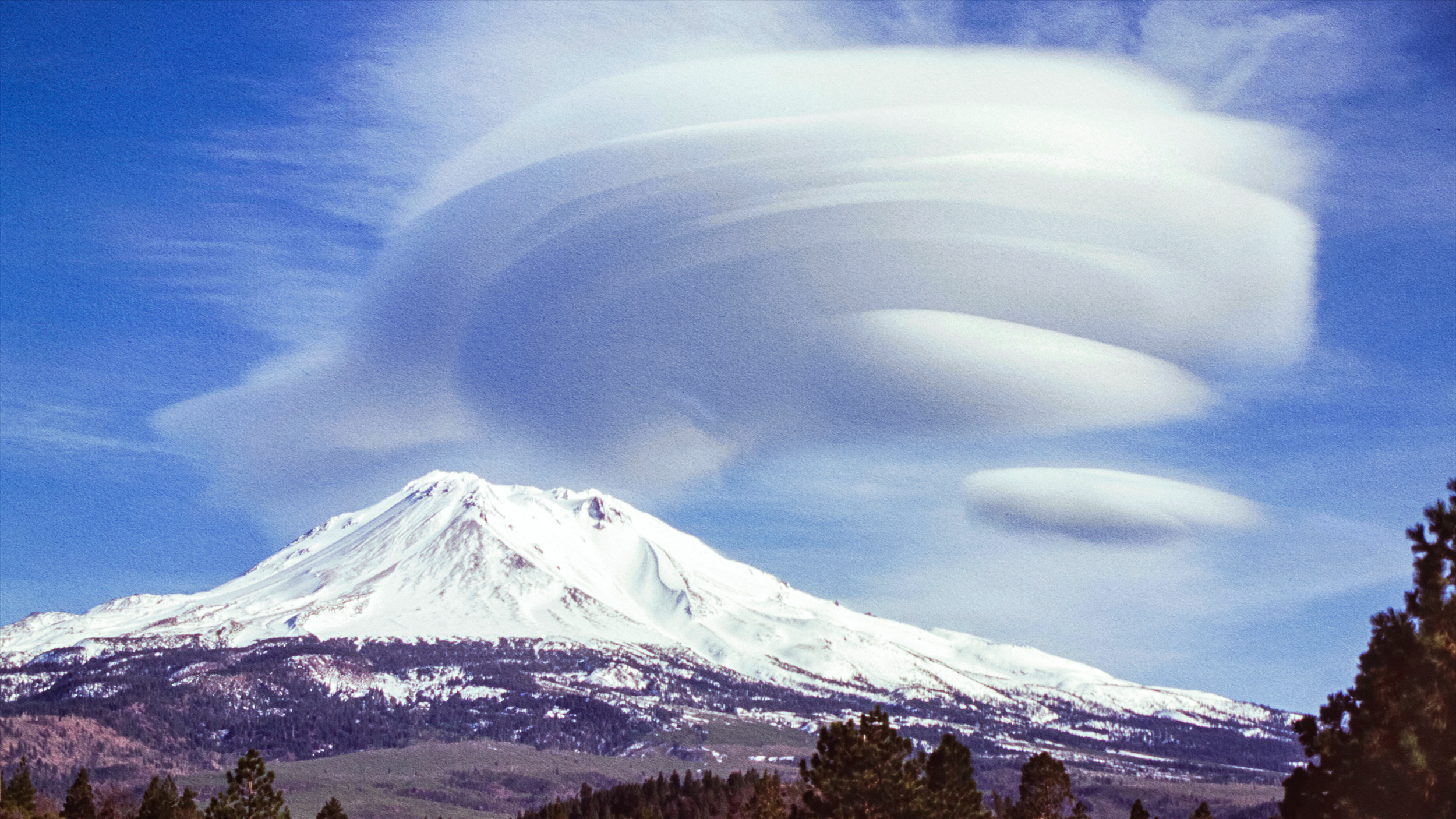 A cloud over Mount Shasta with a mountain in the background.