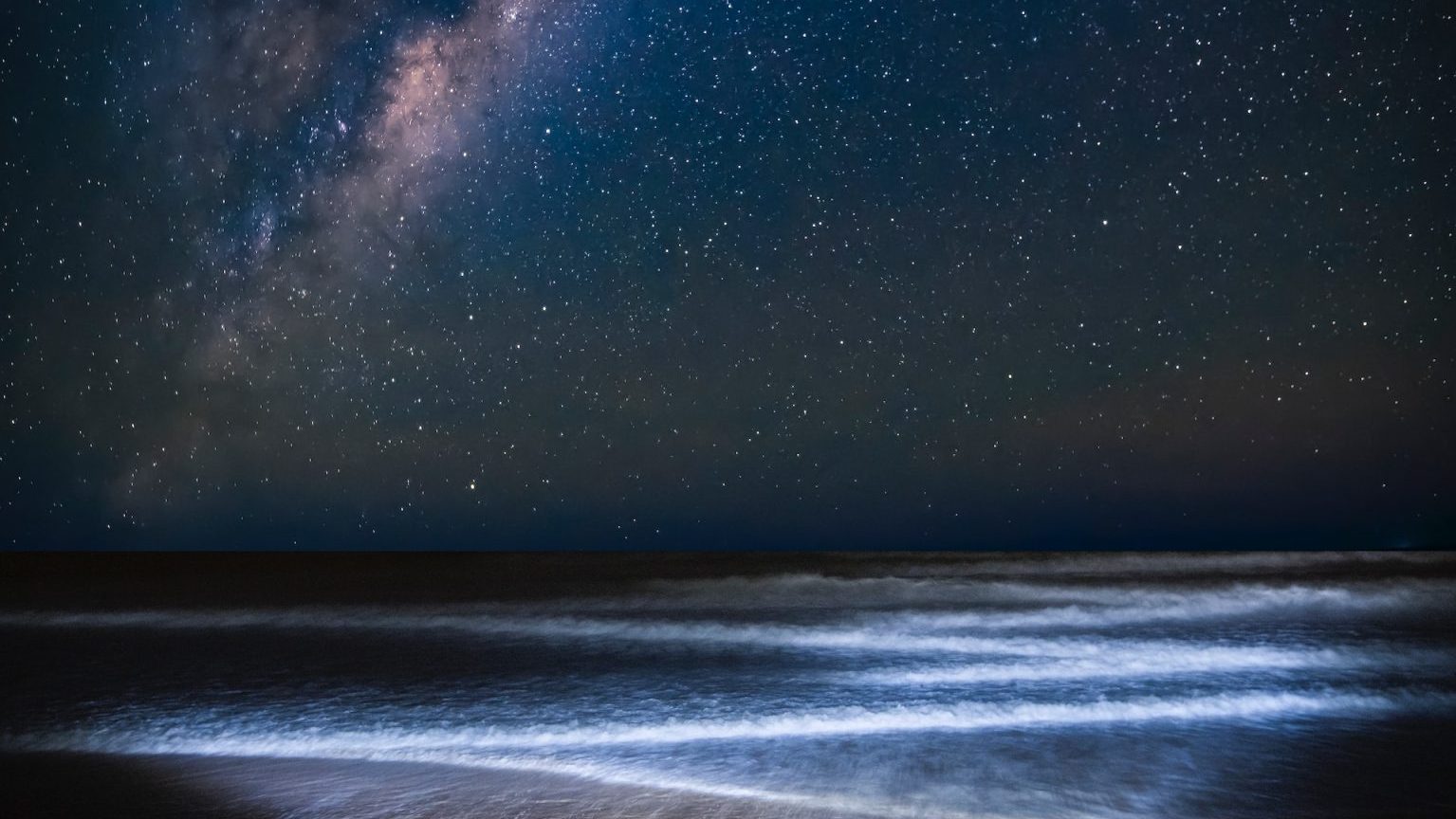 A man standing on a beach under the mysterious milky.