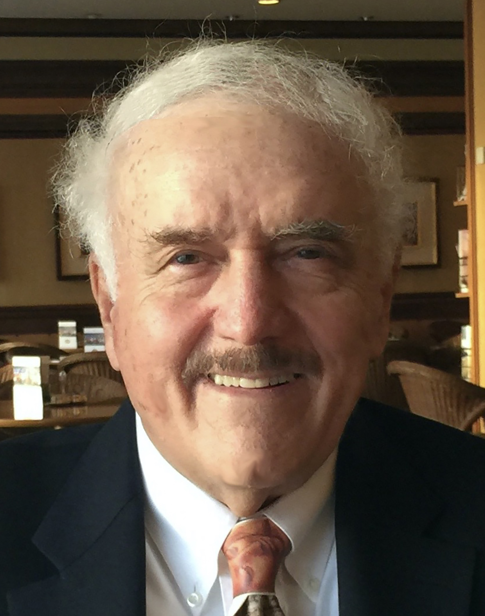 An older man in a suit and tie smiles for the camera.