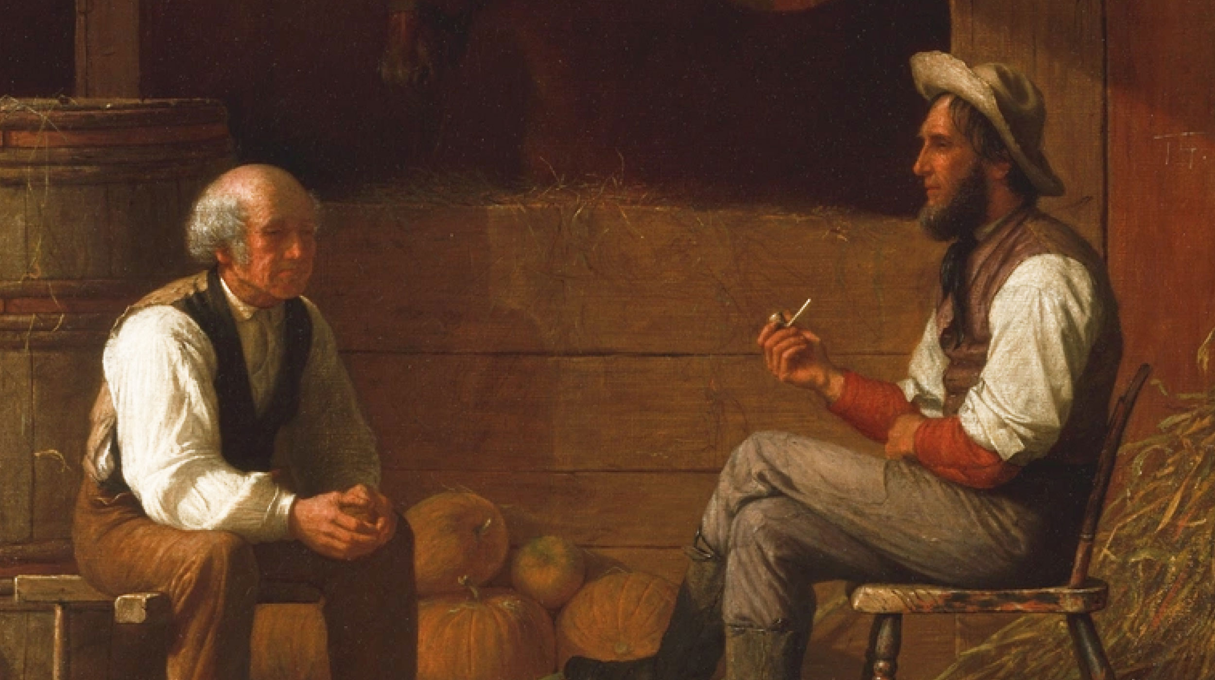 Two men sit facing each other in a barn with pumpkins behind them; one man holds a pipe, and both appear to be engaged in conversation.