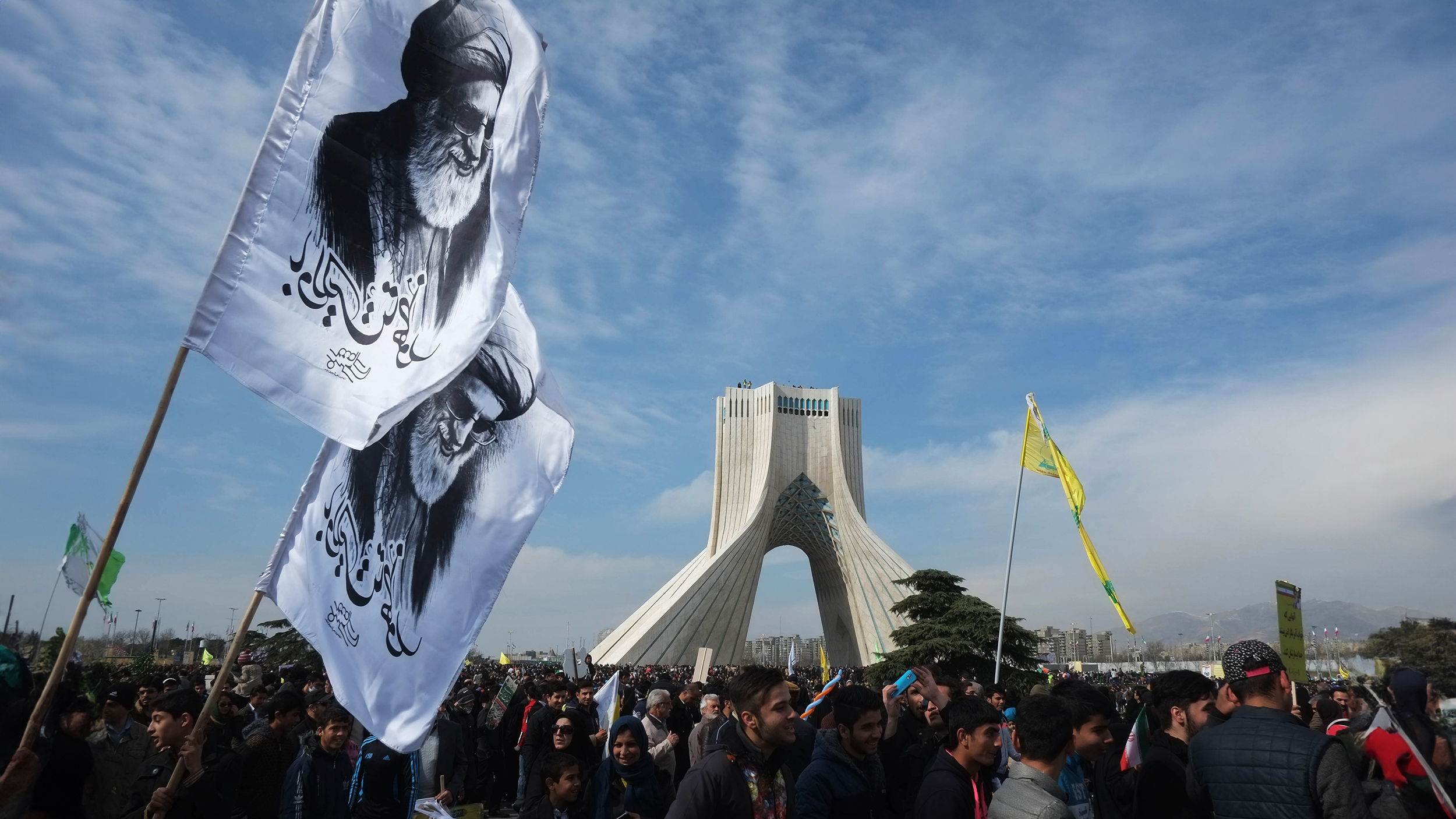 A group of people are holding flags in front of a monument representing democracy.