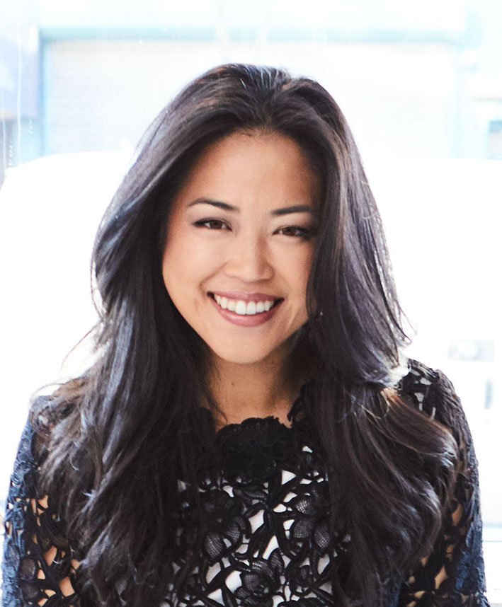 An asian woman smiling in front of a window.