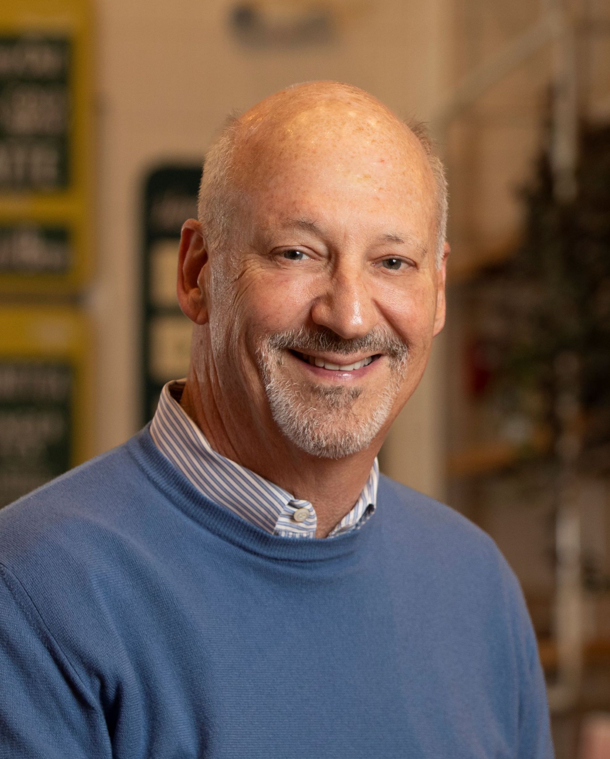 A bald man in a blue sweater smiles in a store.