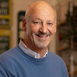 A bald man in a blue sweater smiles in a store.