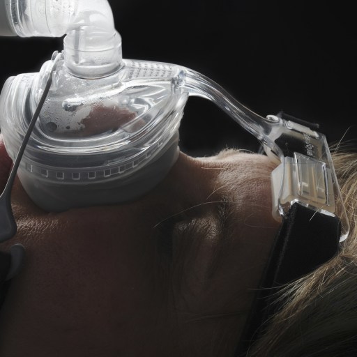 A woman wearing a sleep apnea mask with a bottle of water.