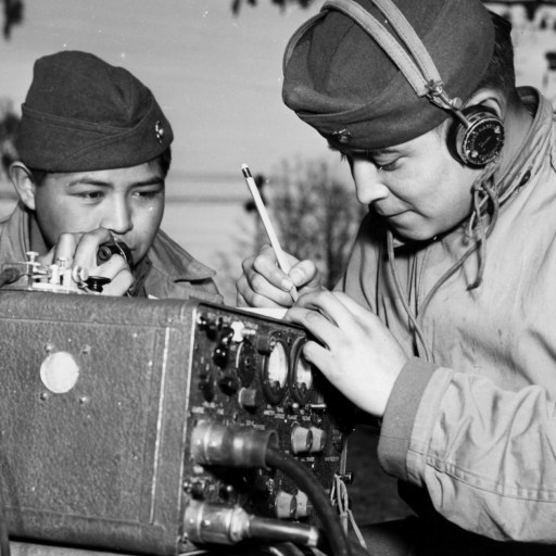 Two navajo men in military uniforms working on a radio.