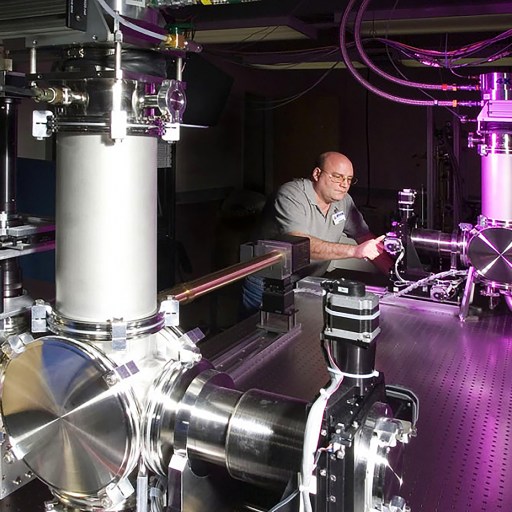 A man is working on a machine in a lab, using laser technology to apply precise pressure.