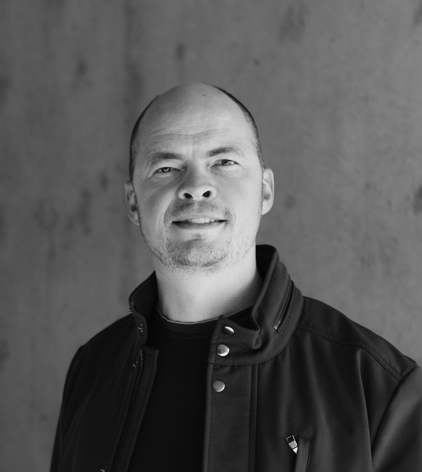 A black and white photo of a bald man smiling.