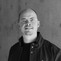A black and white photo of a bald man smiling.