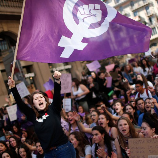 A group of feminists holding a purple flag in front of a crowd.