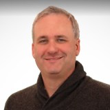 A man in a gray sweater smiles for the camera.