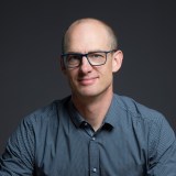 A bald man wearing glasses and a blue shirt.