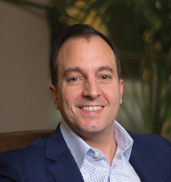 A smiling man in a blue suit sitting on a couch.