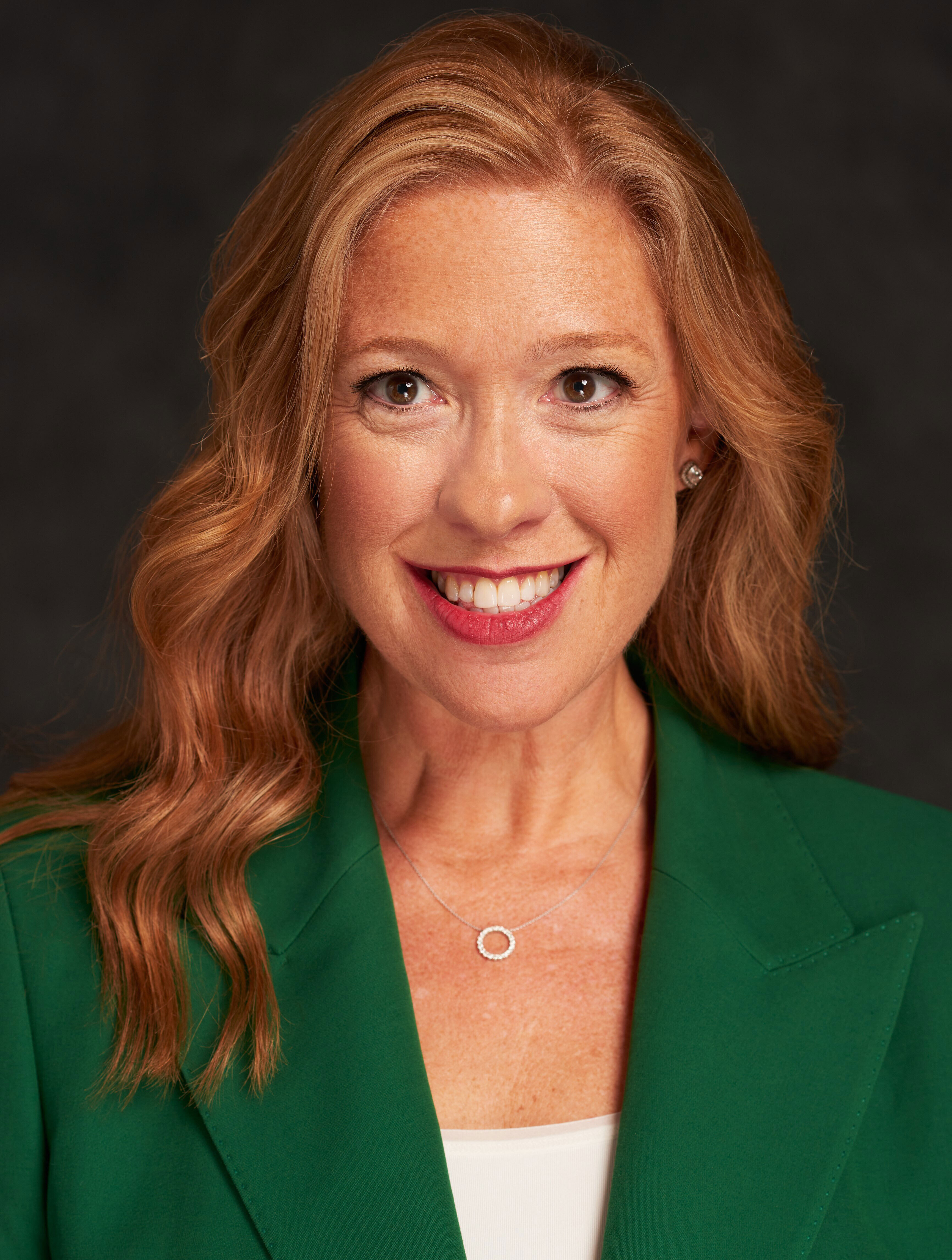 A woman in a green blazer smiling.