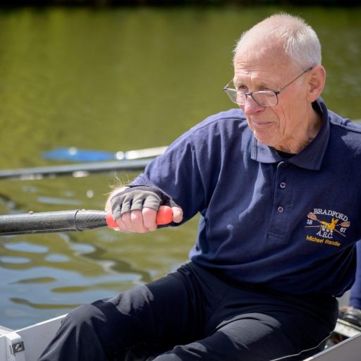 An aging man is rowing in a rowing boat, showcasing his strength despite potential muscle loss.