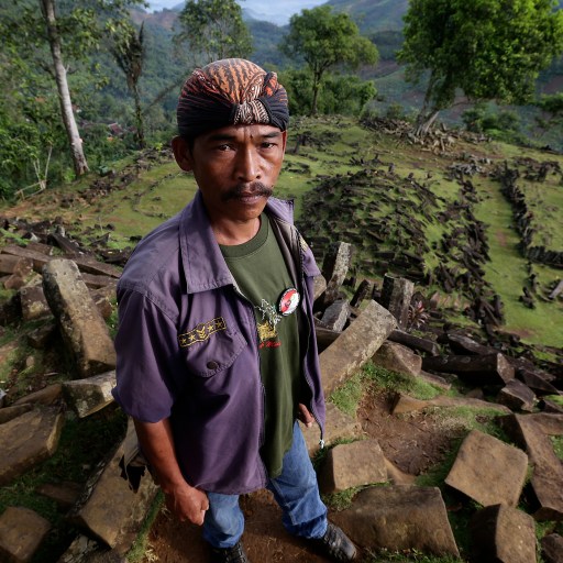 A man standing on top of rocks in the jungle, surrounded by foliage and towering trees.