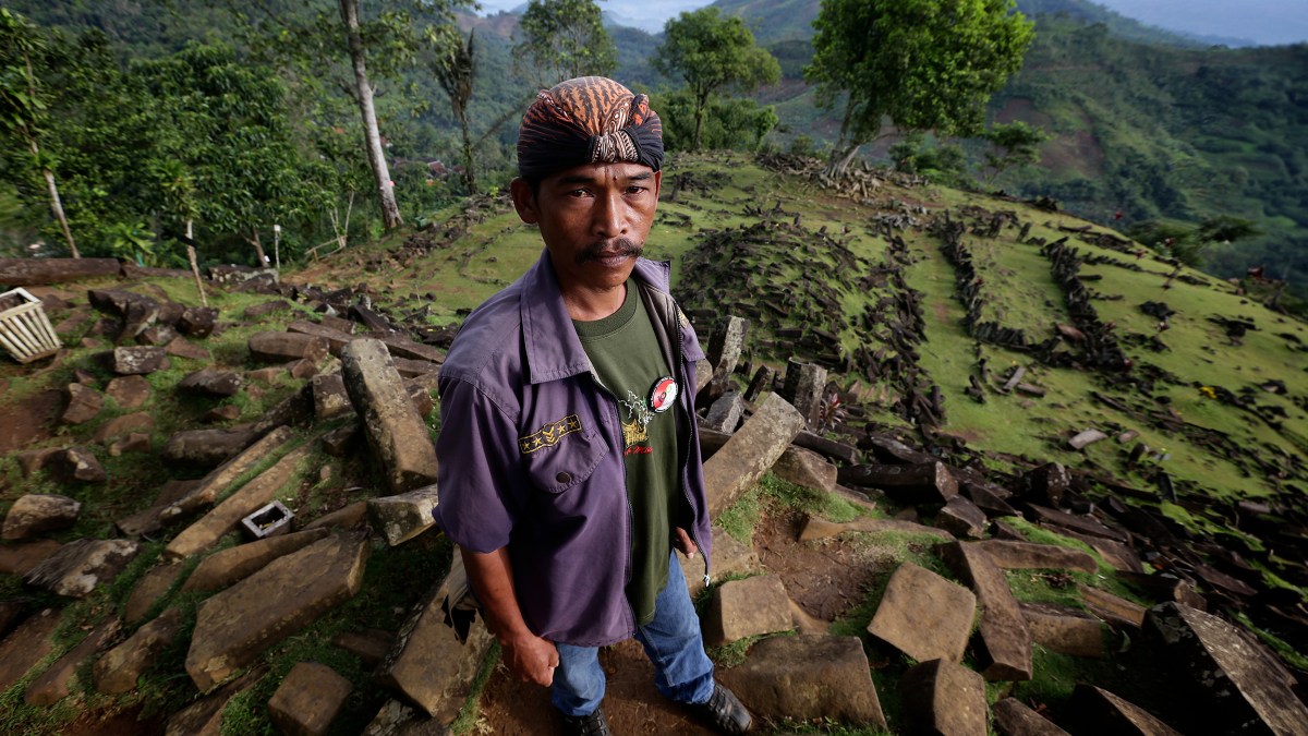 A man standing on top of rocks in the jungle, surrounded by foliage and towering trees.