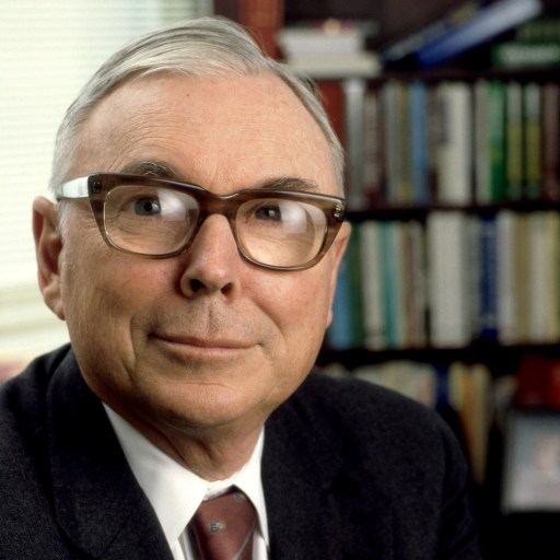 Charles Munger, a man in glasses, sitting in front of a bookcase filled with puzzles.