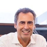 A smiling man in a white shirt sitting at a table.