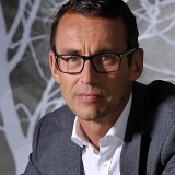 A man in glasses sitting in front of a tree.