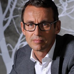 A man in glasses sitting in front of a tree.