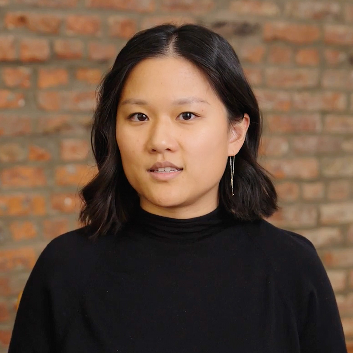 A woman in a black top standing in front of a brick wall.