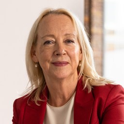 A woman in a red blazer is sitting in front of a window.