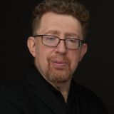 A man with glasses and a beard is posing for a photo.