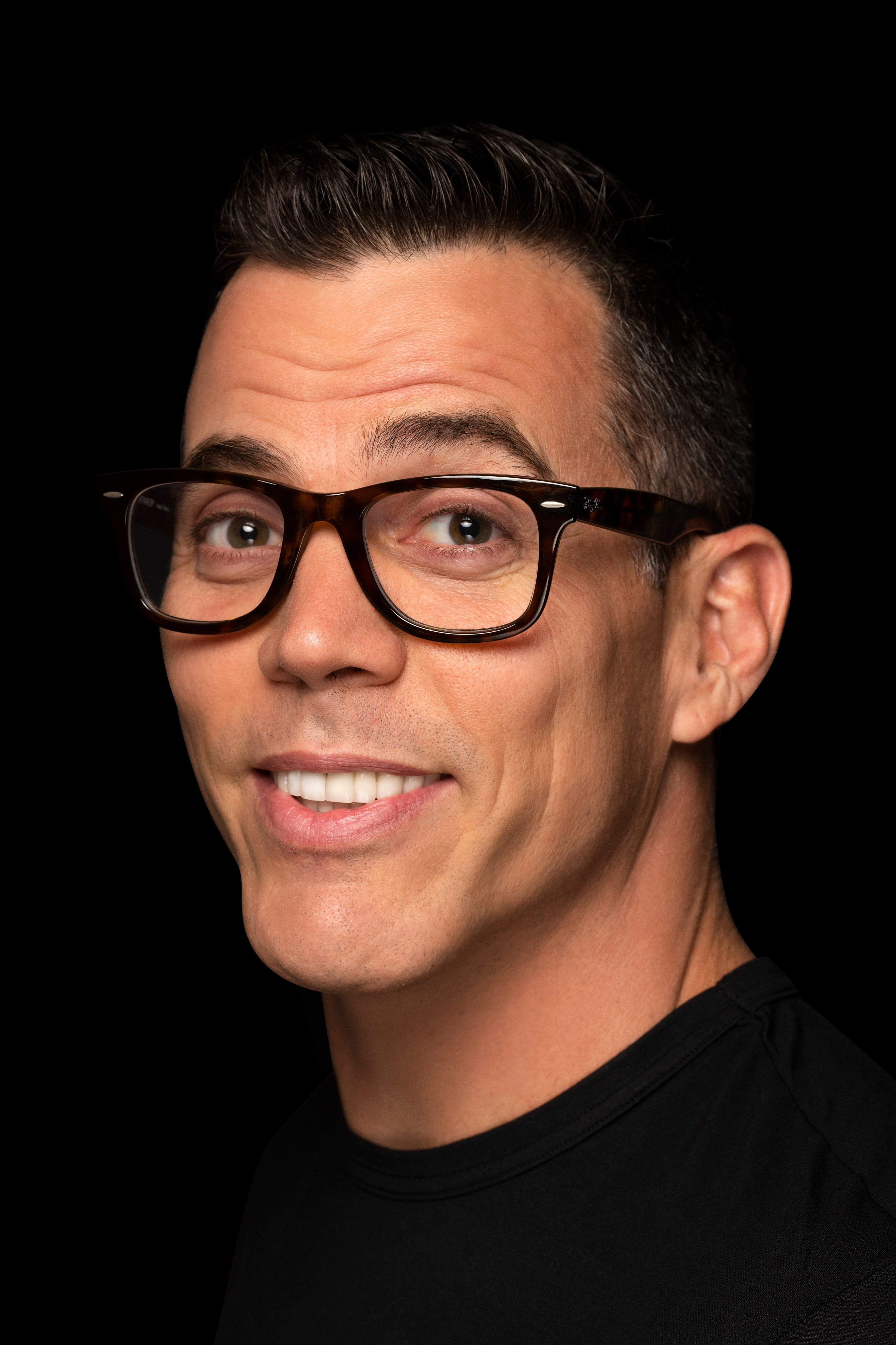 A man in glasses smiling in front of a black background.