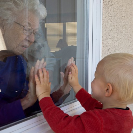 A little boy finding lockdown compensation by reaching out to an old lady through a window.