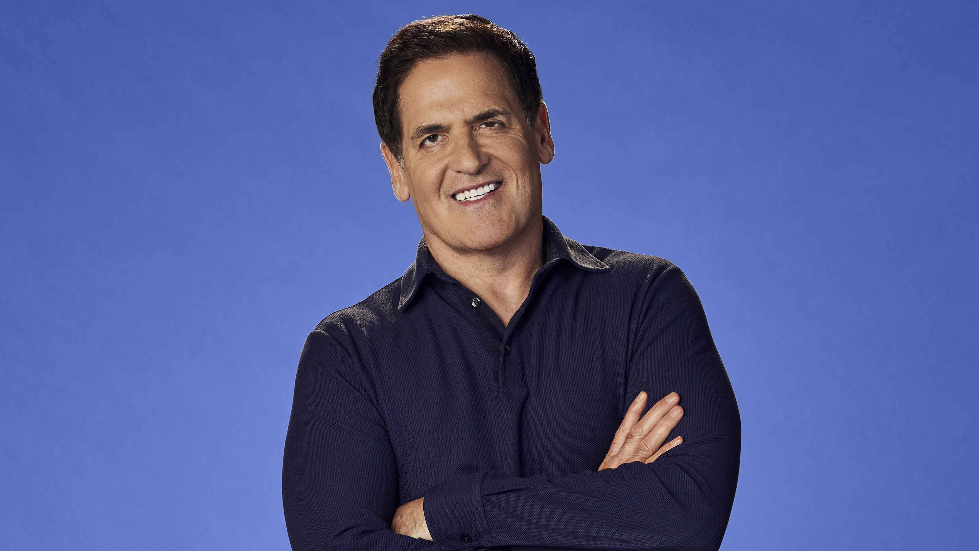 A successful man standing with his arms crossed in front of a vibrant blue background.