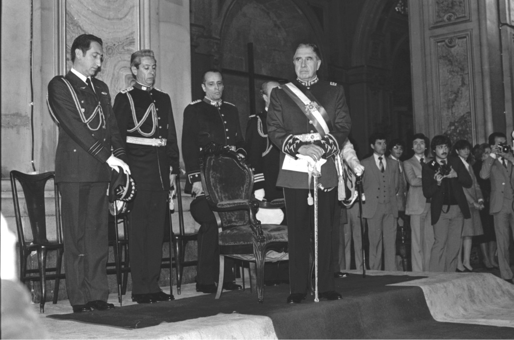 A black and white photo of a group of men standing on a stage, discussing free trade.