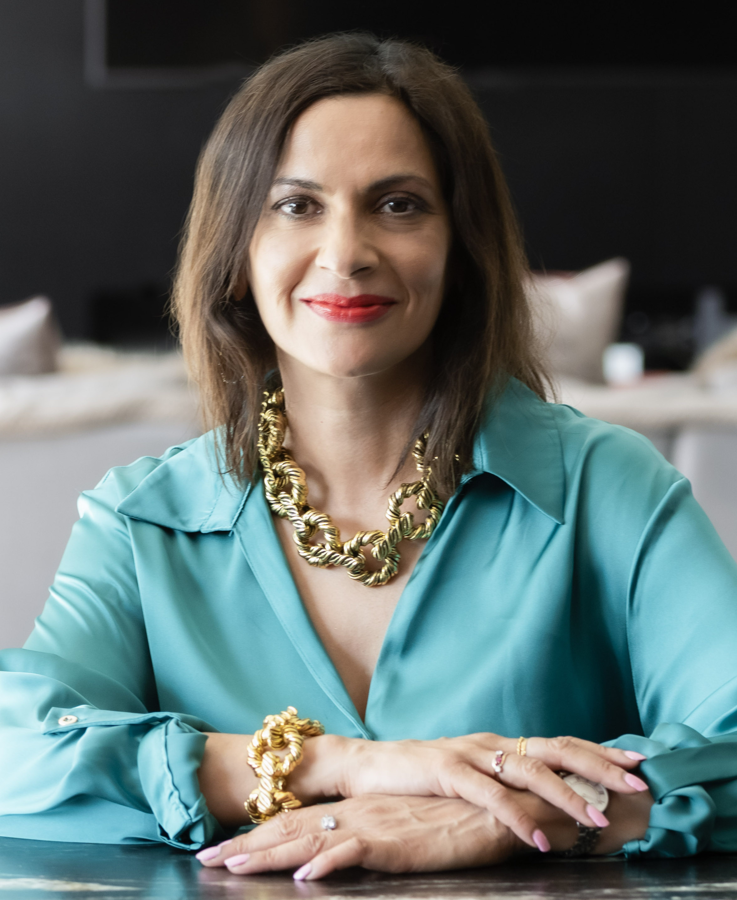 A woman wearing a blue shirt and gold necklace.